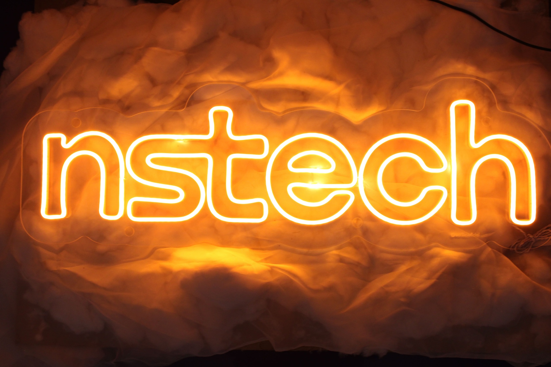 Logo nstech em neon laranja sobre nuvens